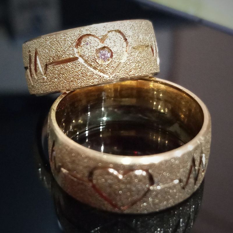 Alianças personalizadas em ouro com coração e batimento cardíaco gravados e pedra rosa