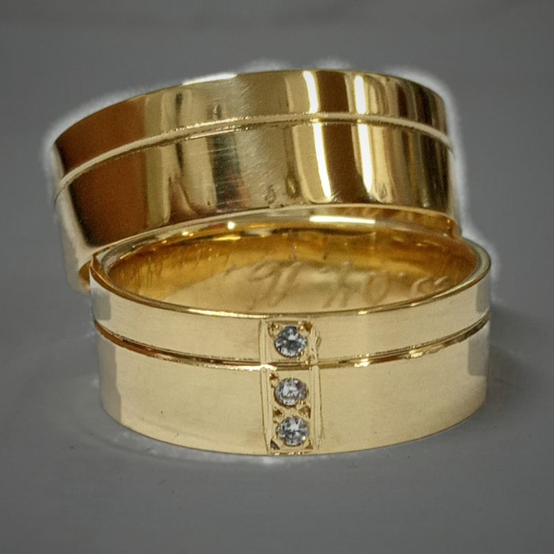 Alianças personalizadas em ouro polido com friso e três pedras na aliança feminina, com gravação interna